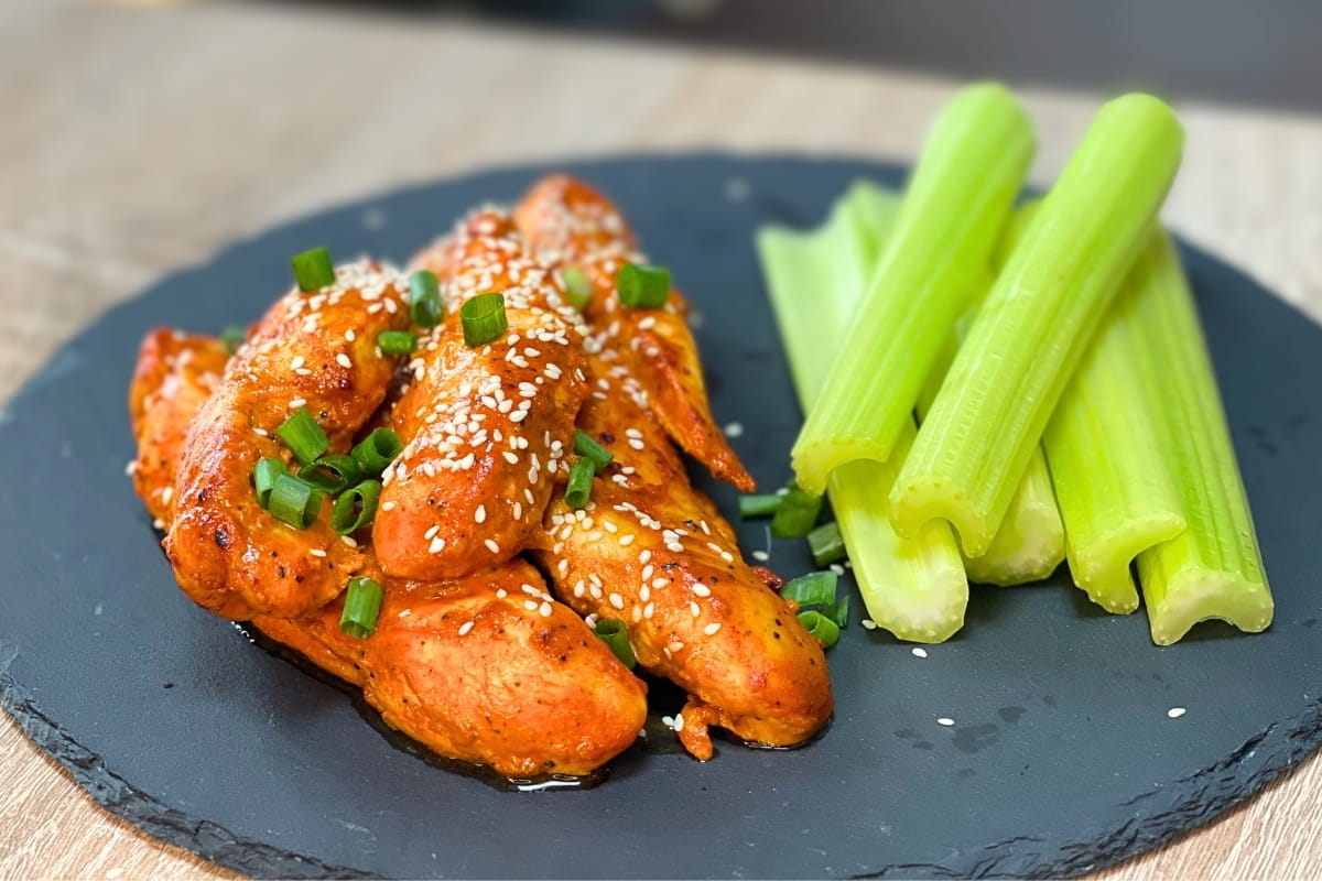 High-Protein Buffalo Chicken Tenders served on a stone plate with fresh celery sticks