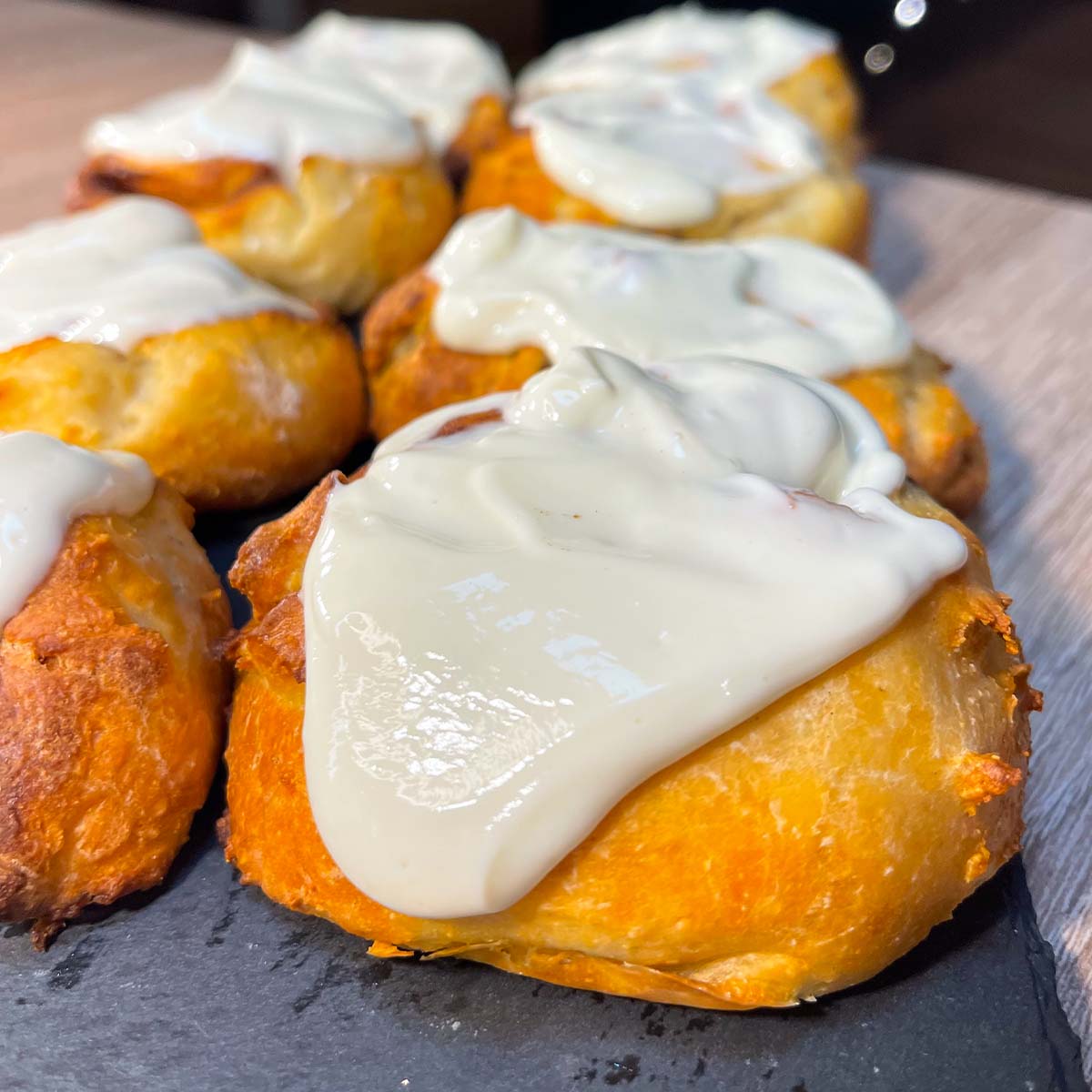Close-up photo of High-Protein Cinnamon Rolls with cream cheese frosting, served on a stone plate