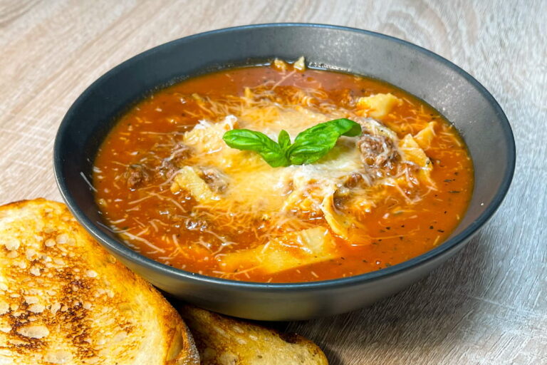 High-Protein Lasagna Soup topped with Parmesan, fresh basil leaves and served with toasted sourdough bread