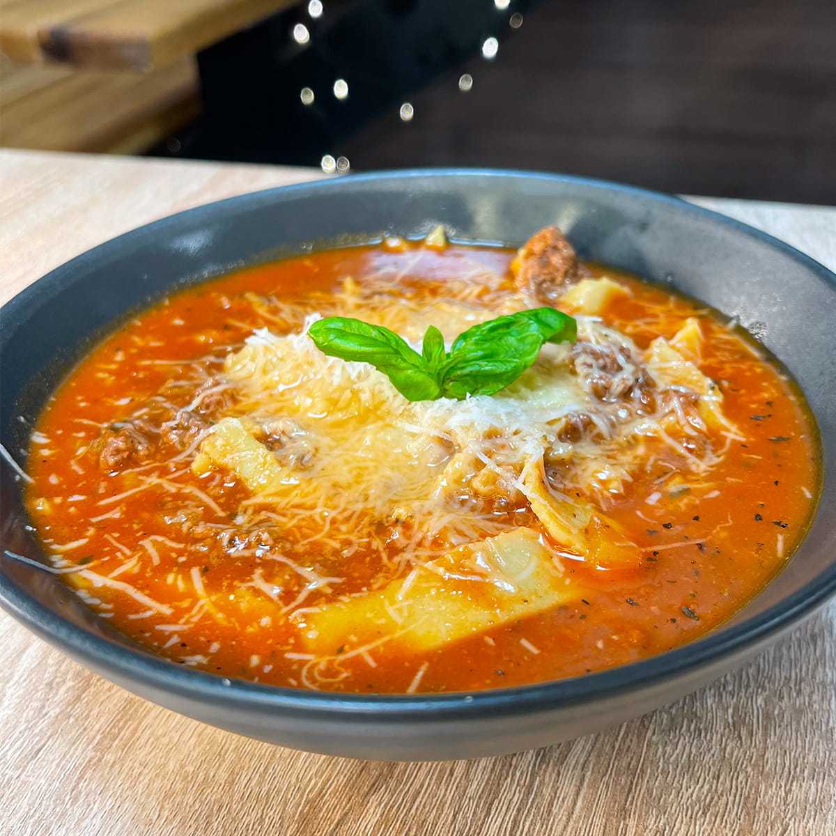 Close-up photo of High-Protein Lasagna Soup topped with Parmesan and fresh basil leaves
