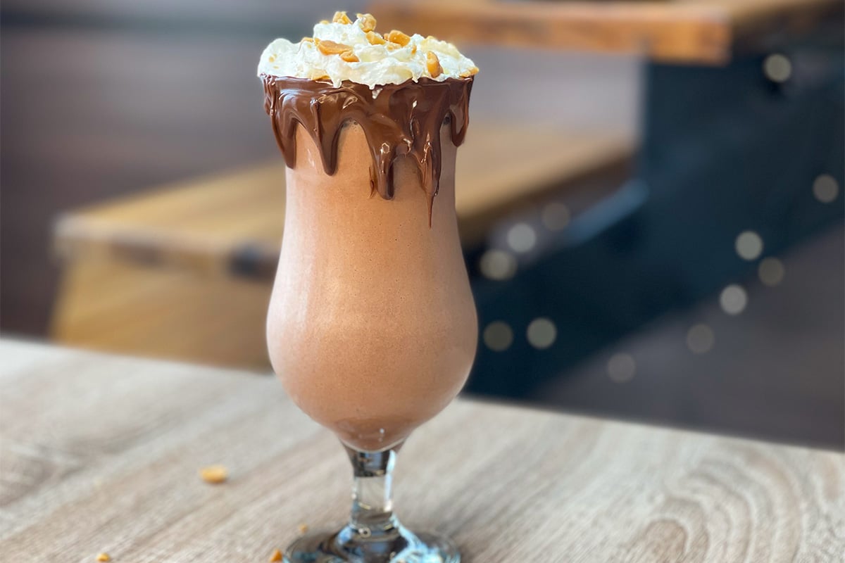 Snickers Protein Shake served in a glass, with light whipped cream, crushed salted peanuts and a chocolate rim (drink idea)