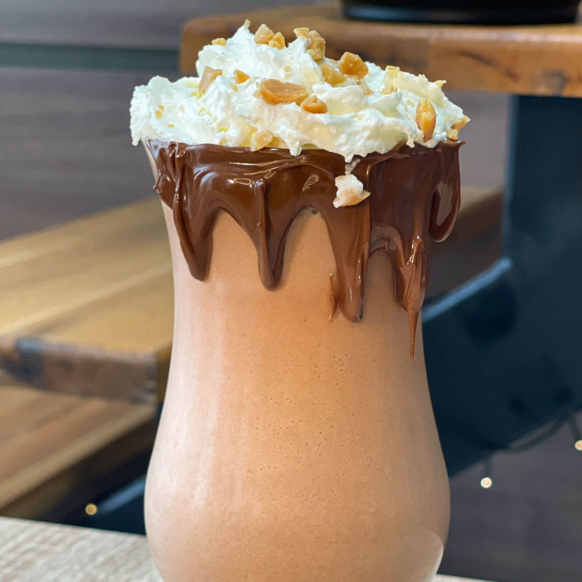 Close-up photo of Snickers Protein Shake served in a glass, with light whipped cream, crushed salted peanuts and a chocolate rim