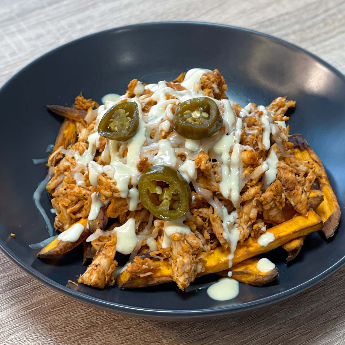 Close-up photo of Loaded Sweet Potato Fries with BBQ, pulled chicken, cheese, honey mustard sauce and sliced jalapeƱos