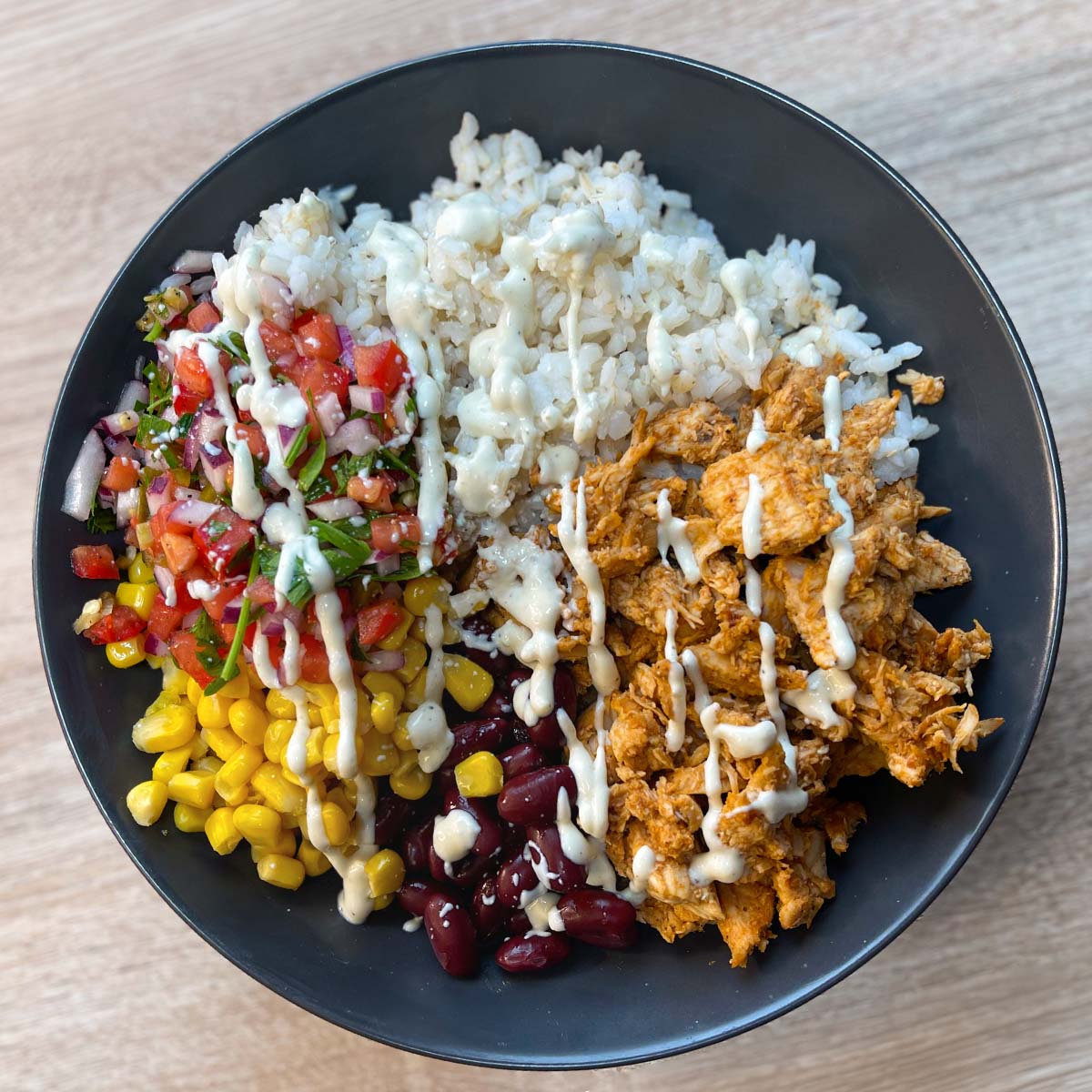 Close-up photo of a Meal Prep BBQ Chicken Burrito Bowl with rice, homemade pico de gallo, corn, kidney beans, BBQ pulled chicken and burrito bowl dressing