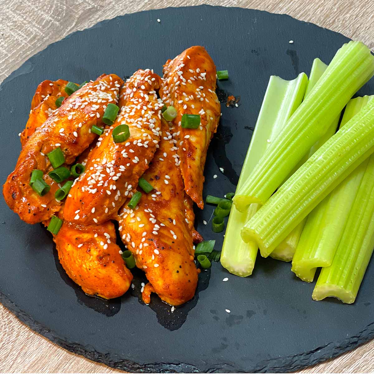 Close-up of Air Fryer Buffalo Chicken Tenders without breading served with celery sticks on a stone plate.