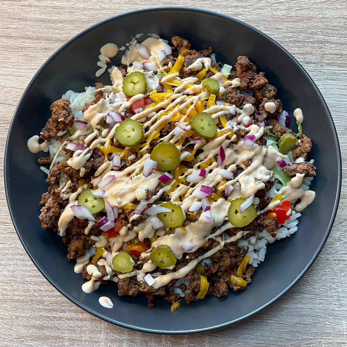 Close-up photo of a Cheeseburger Bowl with rice, ground beef, shredded cheddar cheese, lettuce, tomatoes, pickles, onions and burger sauce