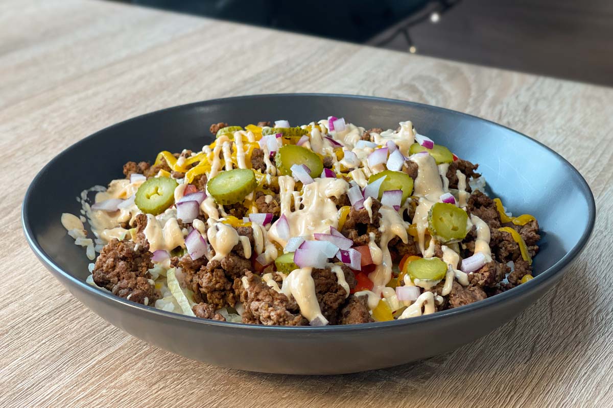 Cheeseburger Bowl with rice, ground beef, shredded cheddar cheese, lettuce, tomatoes, pickles, onions and burger sauce
