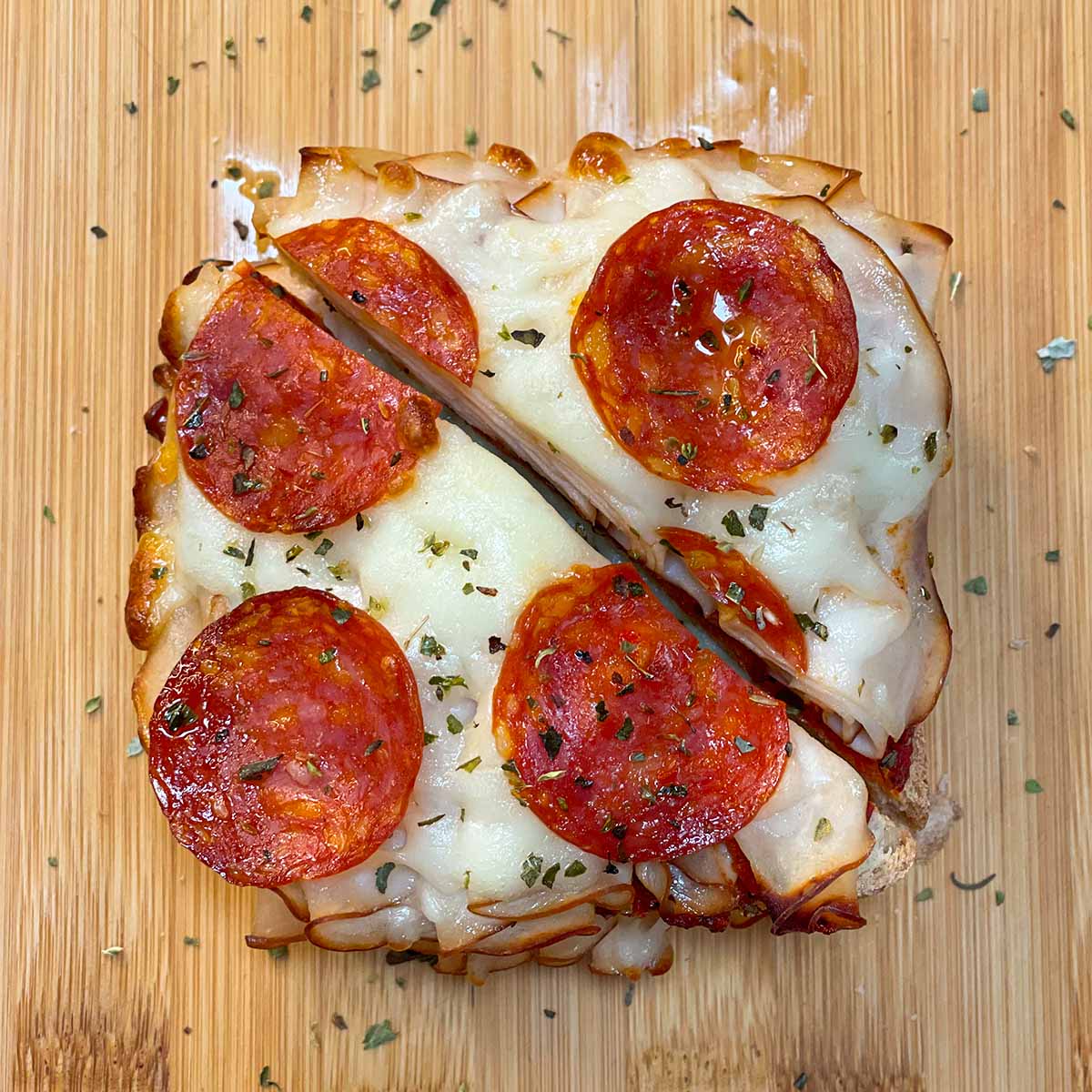 Top-down view of a gourmet pizza grilled cheese sandwich cut diagonally in half, showing melted cheese and sliced pepperoni on top.