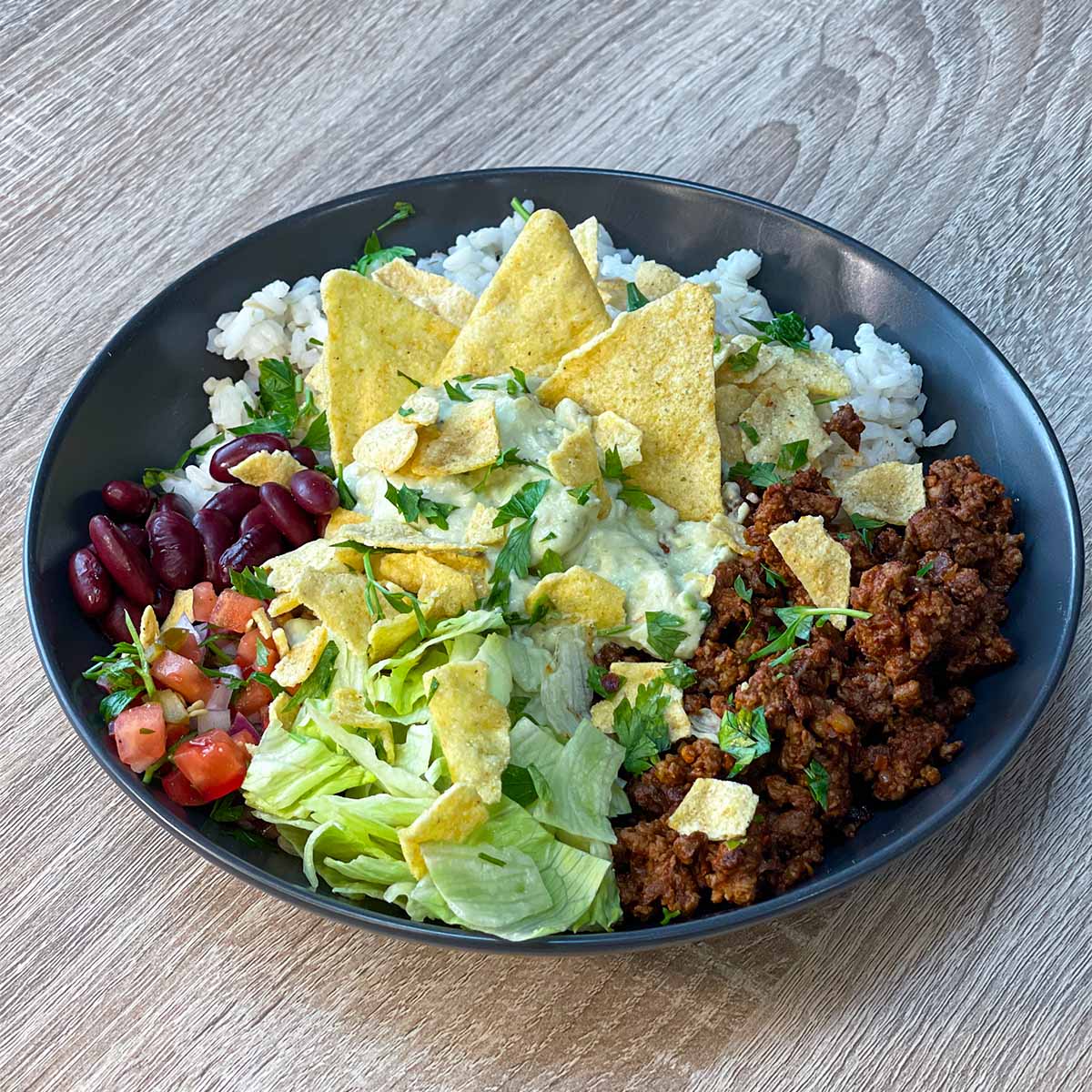 Top-down view of a completed high-protein beef burrito bowl in a black dish, featuring seasoned ground beef, rice, beans, and fresh toppings.