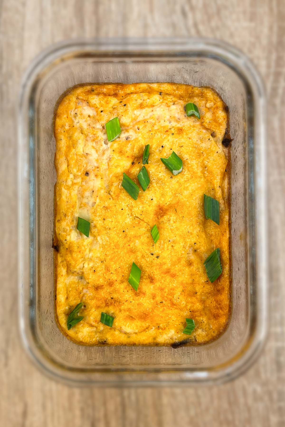 Top-down view of a single baked hash brown and egg breakfast meal prep bowl in a rectangular glass container, garnished with chopped green spring onions.