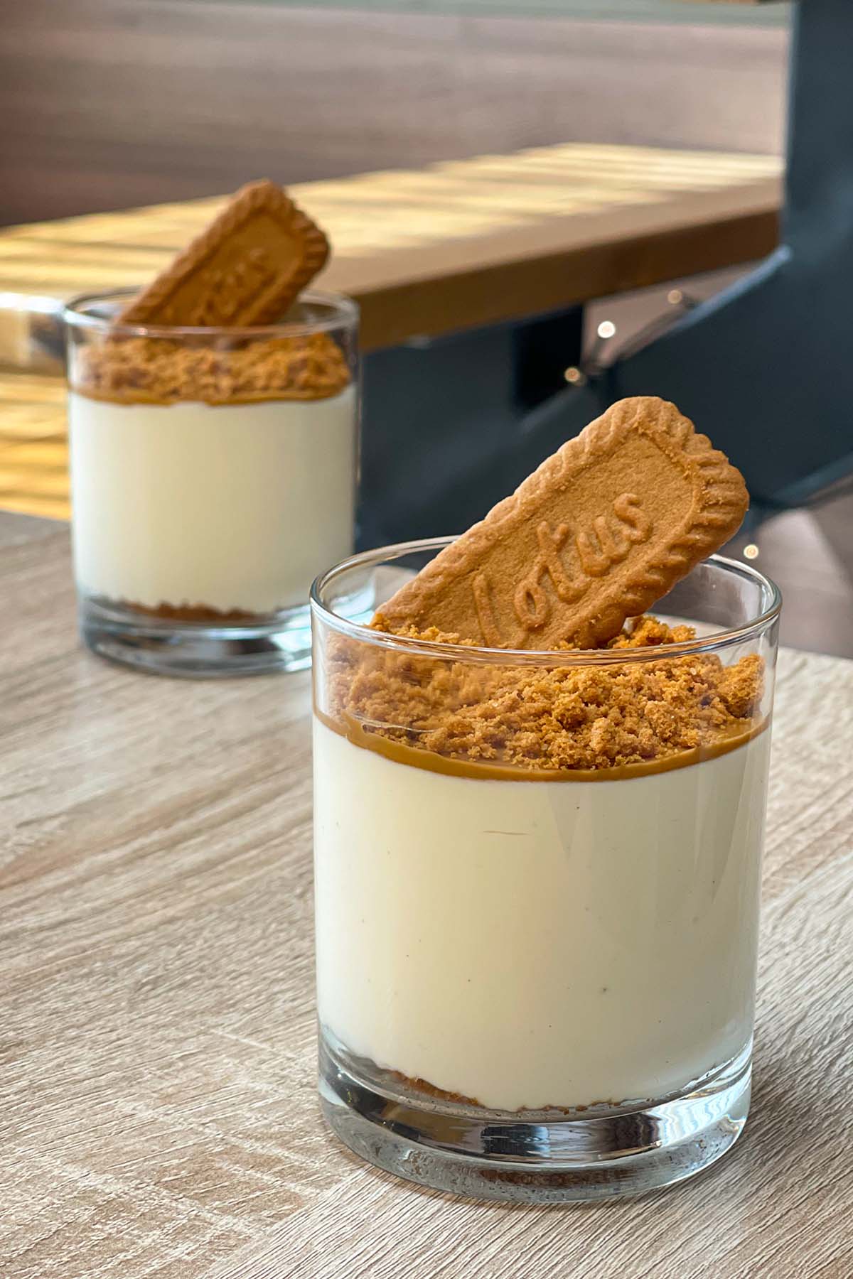 Portrait shot of two no-bake Biscoff cheesecake cups layered with a biscuit base, cheesecake filling, cookie butter spread, crushed biscuits, and a whole Lotus Biscoff cookie.