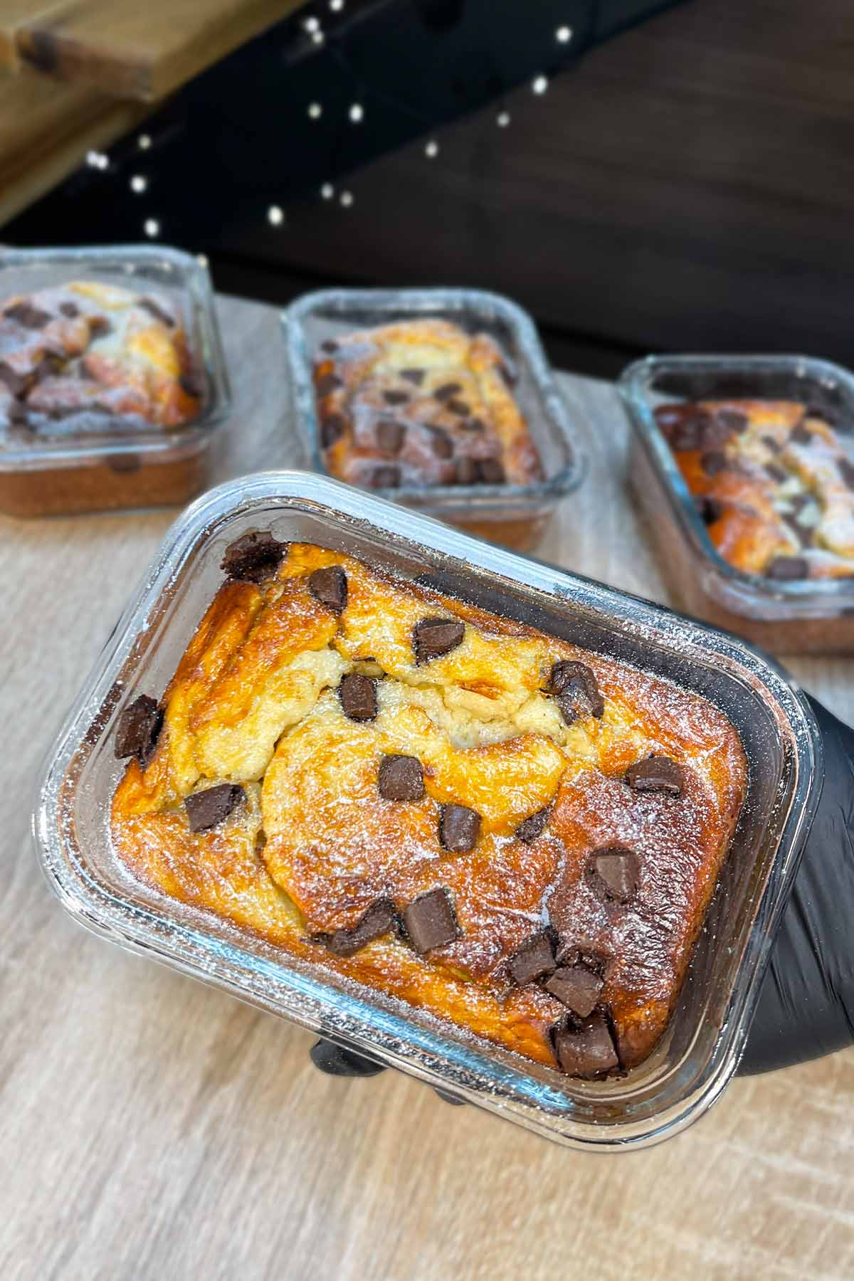 Top-down view of a single chocolate chip protein pancake bowl held up in a glass meal prep container with three other bowls blurred in the background.