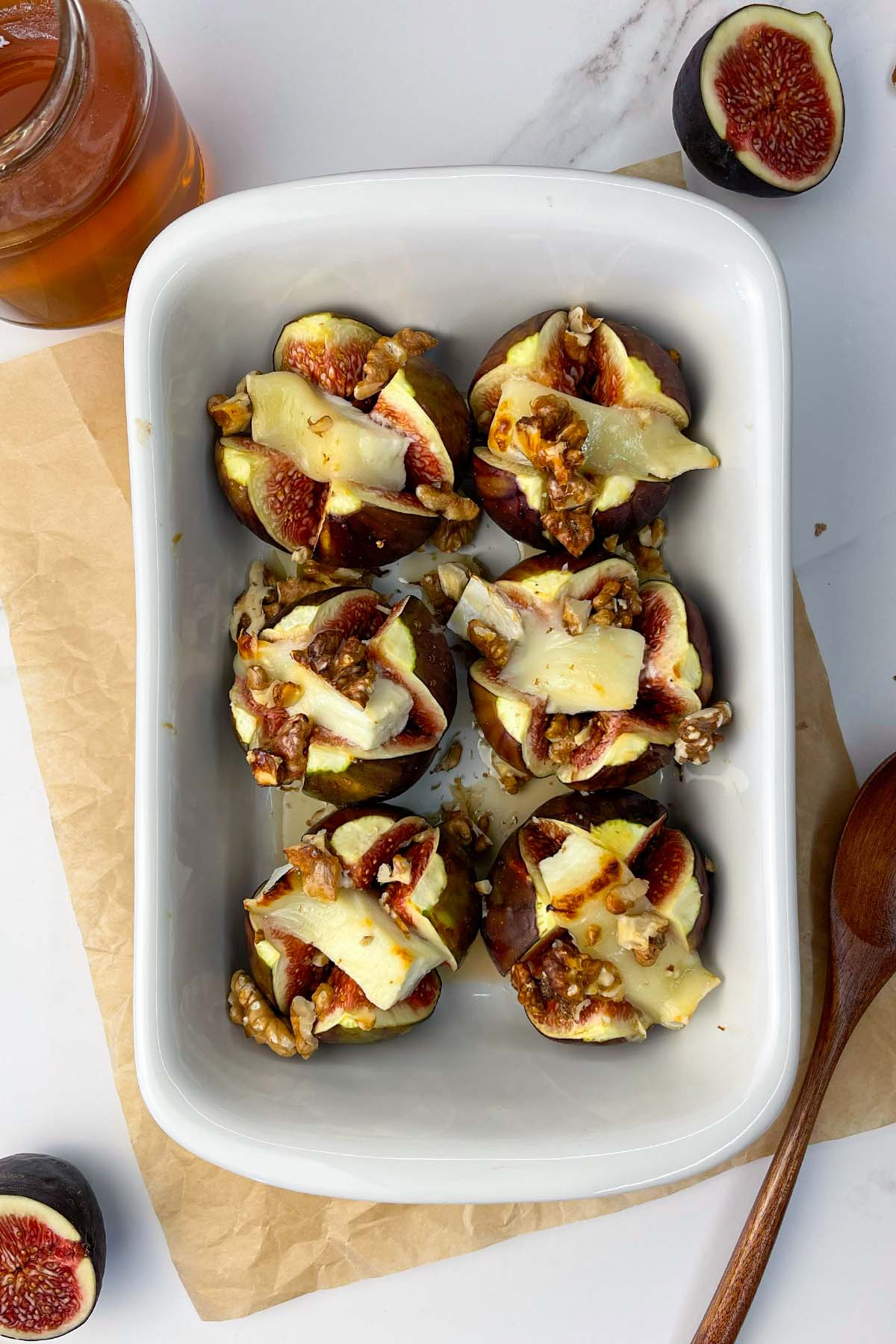 Top-down view of six completed baked figs with goat cheese and walnuts in a white rectangular baking dish, ready to be served.