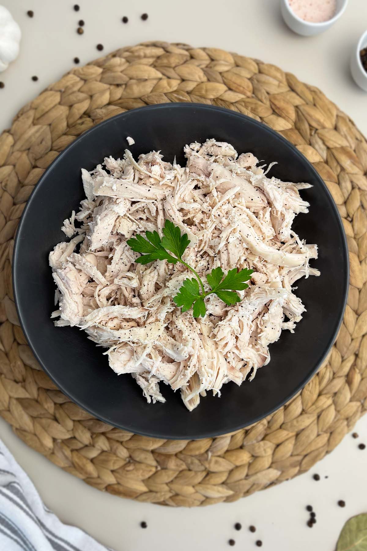 Top-down hero shot of shredded chicken in a dark dish, resting on a round woven placemat.