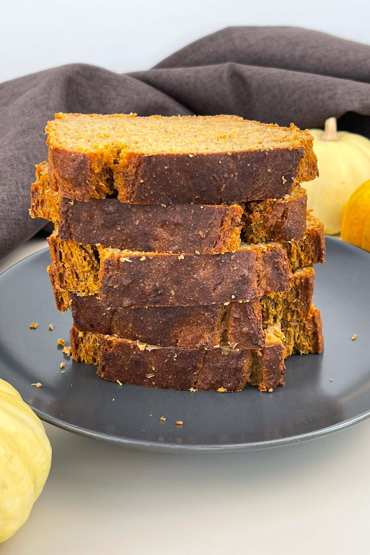Vertical close-up stack of sliced pumpkin banana bread on a dark gray plate, garnished with small decorative pumpkins in the background.